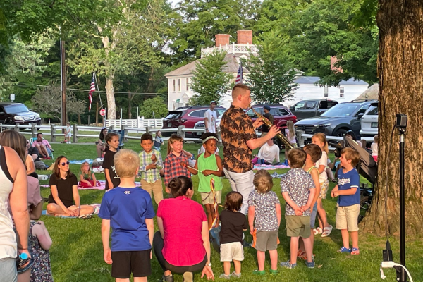Children following Mr. Aaron while he plays the saxophone at the summer reading kick off concert on the village green